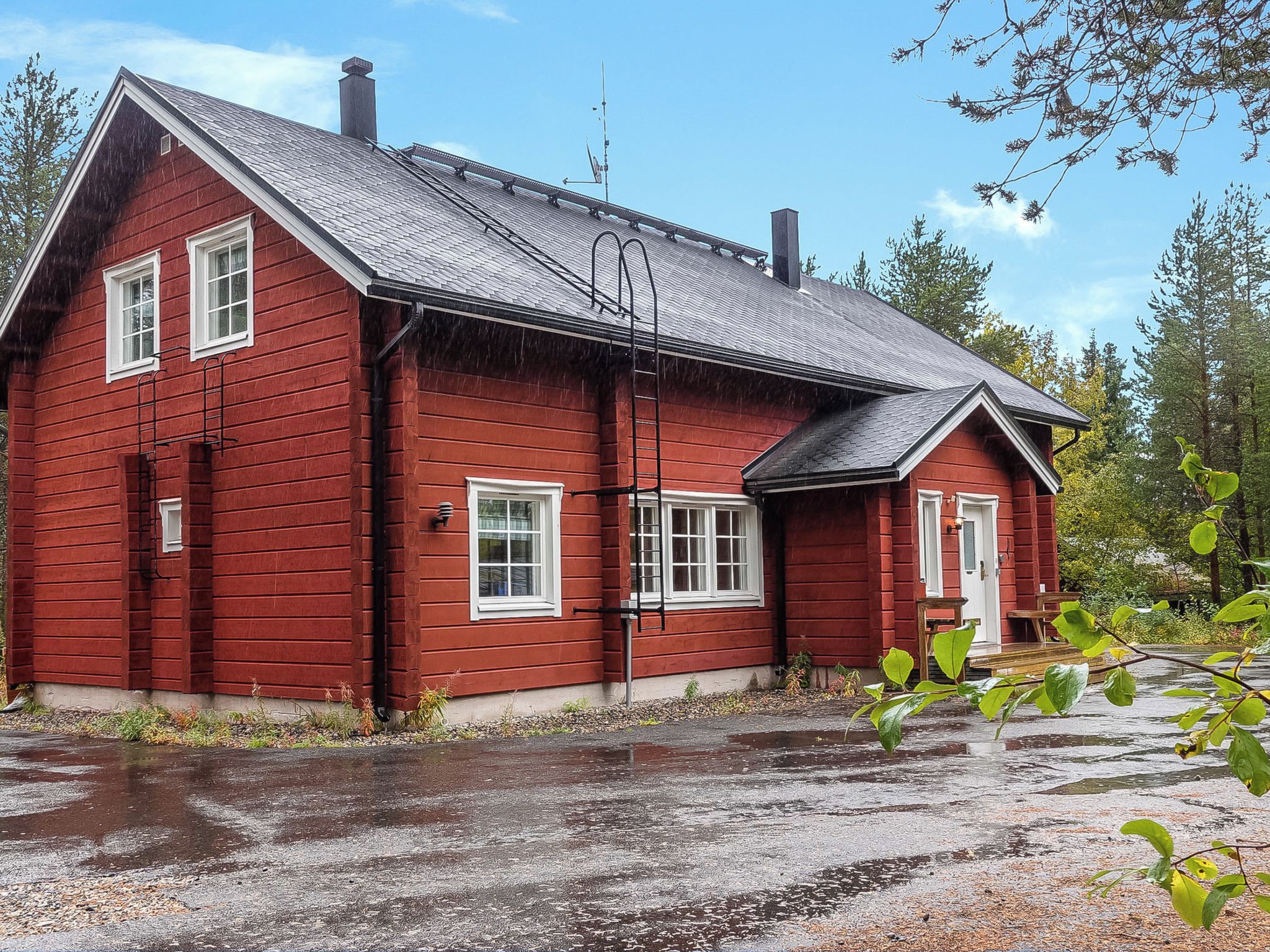 A red wooden house with a sloped roof, a chimney, and a small porch with a bench.