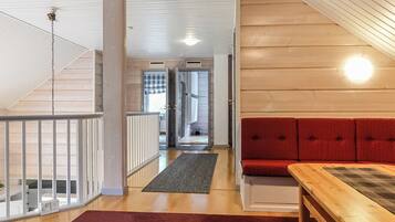 A wooden interior with a red sofa, a wooden table, and a staircase leading to another room.