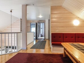 A wooden interior with a red sofa, a wooden table, and a staircase leading to another room.