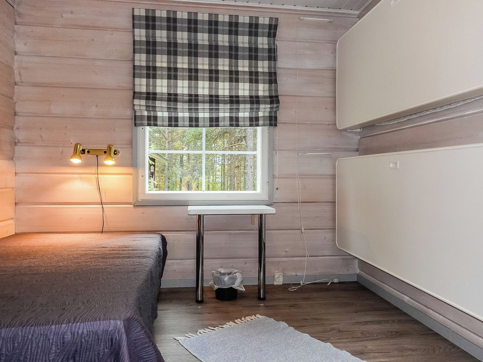 A room with a bed, a table, a window with a view of trees, and a radiator.