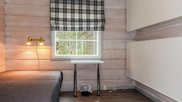 A room with a bed, a table, a window with a view of trees, and a radiator.