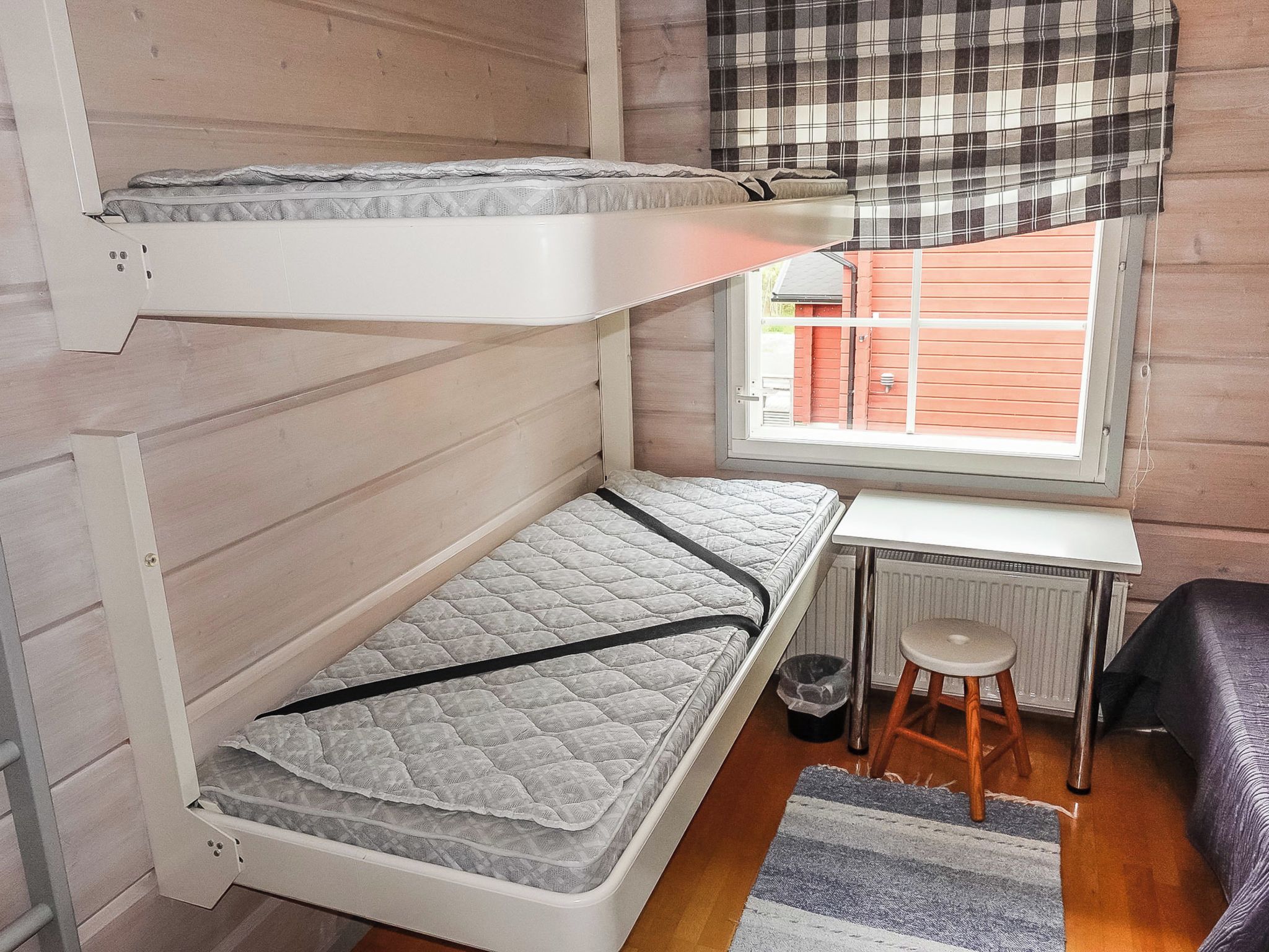 A compact room with a bunk bed, a small desk, a radiator, and a window with a view of the outside.
