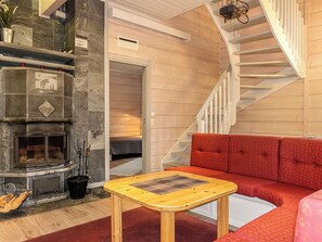 A cozy living room with a fireplace, a red sofa, a wooden coffee table, and a staircase.