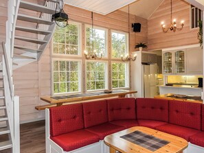 A cozy cabin interior with a red cushioned bench, a wooden table, and a staircase.