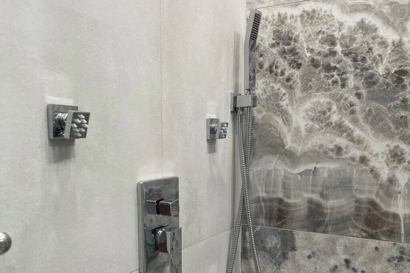 A bathroom with a shower, a control panel, and a marble wall.