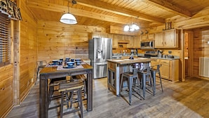 A wooden cabin-style kitchen with a central island, stainless steel appliances, and a dining area with bar stools. - Springtime Specials! Secluded Log Cabin-NEW Hot Tub-Wrap Around Porch (Sevierville)