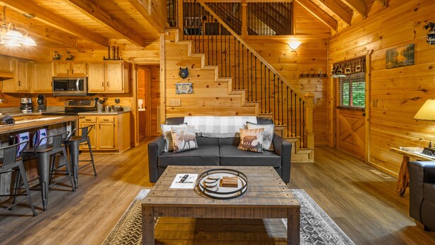 A wooden cabin interior with a kitchen, dining area, and a staircase leading to a loft. - Springtime Specials! Secluded Log Cabin-NEW Hot Tub-Wrap Around Porch (Sevierville)