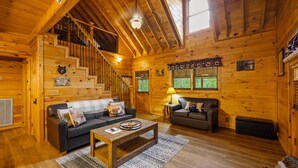 A log cabin interior with a staircase, two sofas, a coffee table, and a window with curtains. - Springtime Specials! Secluded Log Cabin-NEW Hot Tub-Wrap Around Porch (Sevierville)