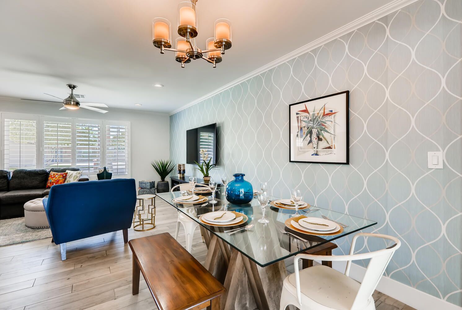 Un coin repas avec une table en verre, des chaises blanches et un vase bleu.