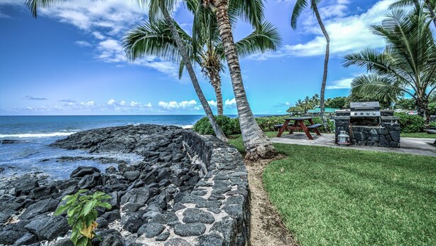 A stone wall, a picnic table, and a grill by the ocean.