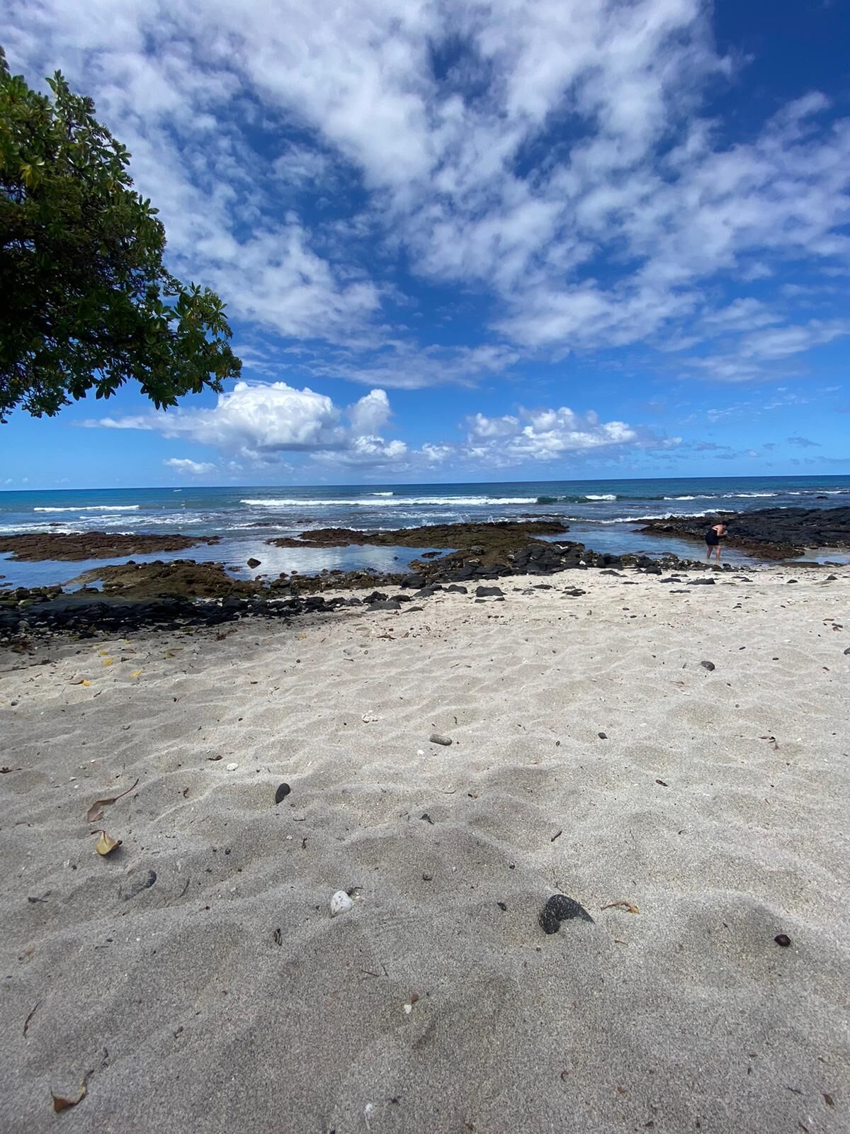 A beach with a clear sky, rocky shoreline, and a person standing near the water.