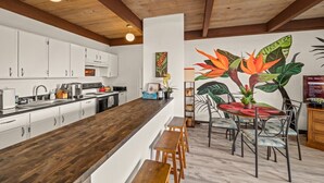 A modern kitchen with white cabinets, a wooden island, and a dining area with a mural of tropical plants.