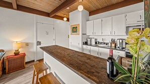 A modern kitchen with white cabinets, a wooden countertop, and a wooden ceiling.