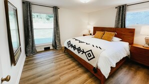 Een slaapkamer met een houten bed, een nachtkastje met een lamp en een raam met gordijnen.