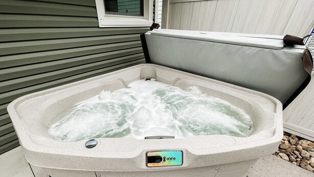 Een hottub met bedieningspaneel, voor een huis met gevelbekleding en een raam.