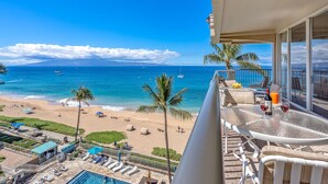 A balcony with a view of a beach and ocean, a pool area, and outdoor seating. - Maui Resort Rentals: The Whaler 701 - Oceanfront 7th Floor 1BR/2A, Sweeping Ocean Views from Lanai to Black Rock and Beyond! (Lahaina)