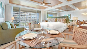 A hotel room with a large bed, a dining area with a glass table, and a view of a building with balconies. - Maui Resort Rentals: The Whaler 315 - Remodeled Interior Courtyard Studio, Gorgeous Ocean Views! (Lahaina)