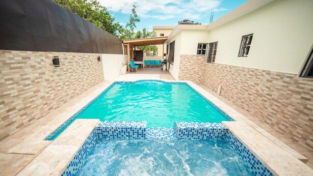 Une piscine rectangulaire aux carreaux de mosaïque bleus, entourée d’un mur de briques et d’un patio couvert.