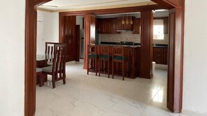 Une cuisine spacieuse avec des meubles en bois, un îlot central doté de tabourets, et un coin repas avec une table et des chaises.