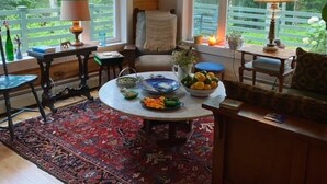 Een gezellige kamer met een ronde tafel, stoelen en uitzicht op een weelderige tuin door grote ramen.