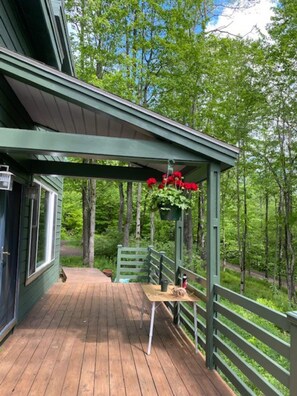 A wooden deck with a green railing, a hanging flower basket, and a bench.