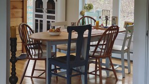 Een eetruimte met een houten tafel en stoelen, een kroonluchter en een raam met uitzicht op bomen.