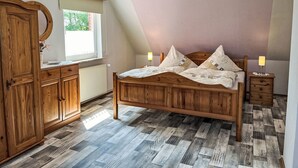 A bedroom with a wooden bed, a dresser, a mirror, and a window with a view of greenery. - Osterkamp by Interhome (Westerholt)