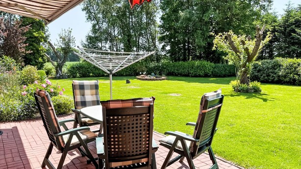 An outdoor patio with a table and chairs, surrounded by a well-maintained lawn and trees. - Osterkamp by Interhome (Westerholt)