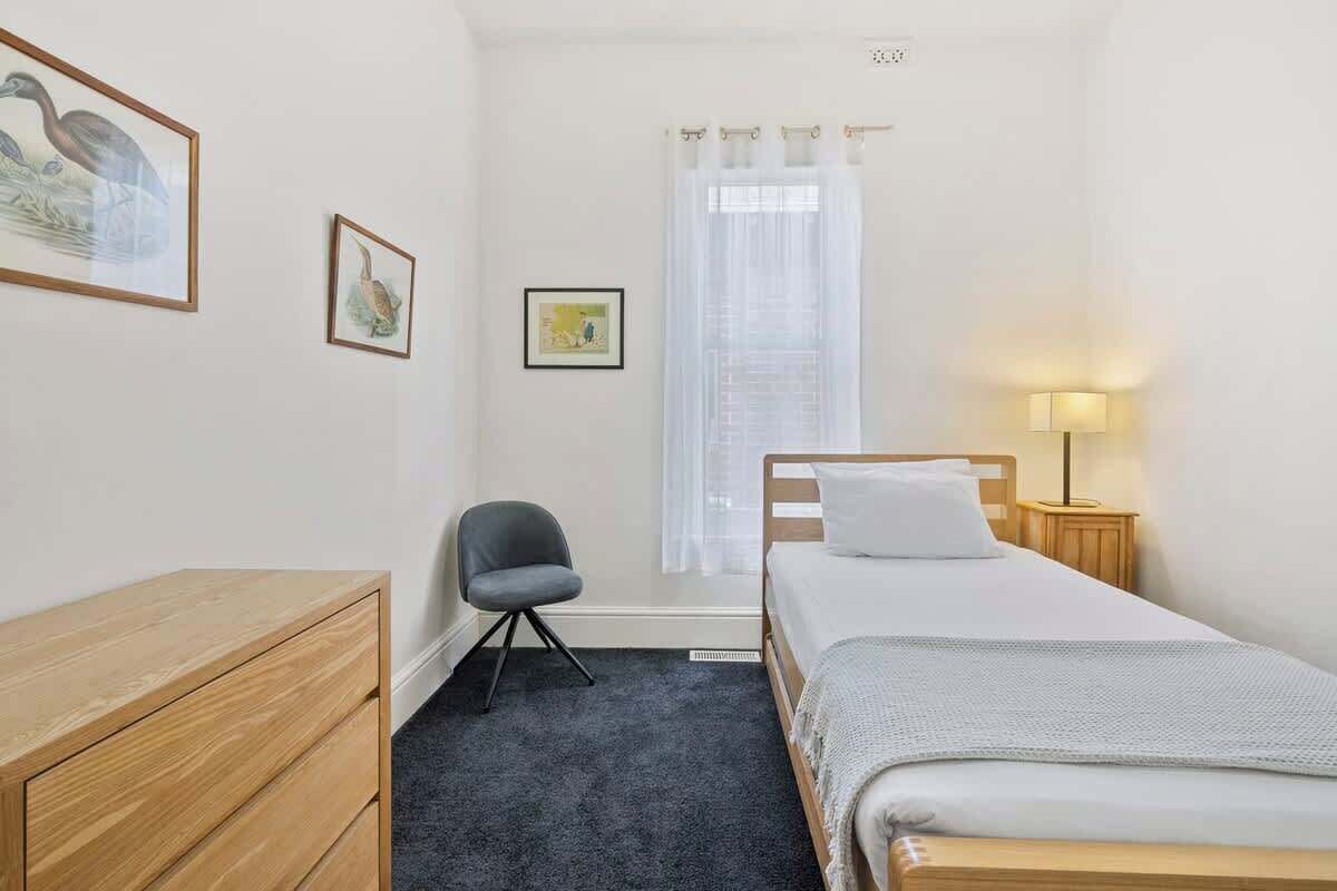 A bedroom with a bed, a chair, a dresser, and a window with curtains.