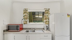 Una cocina compacta con armarios blancos, un lavamanos de acero inoxidable, un microondas rojo y un refrigerador blanco.