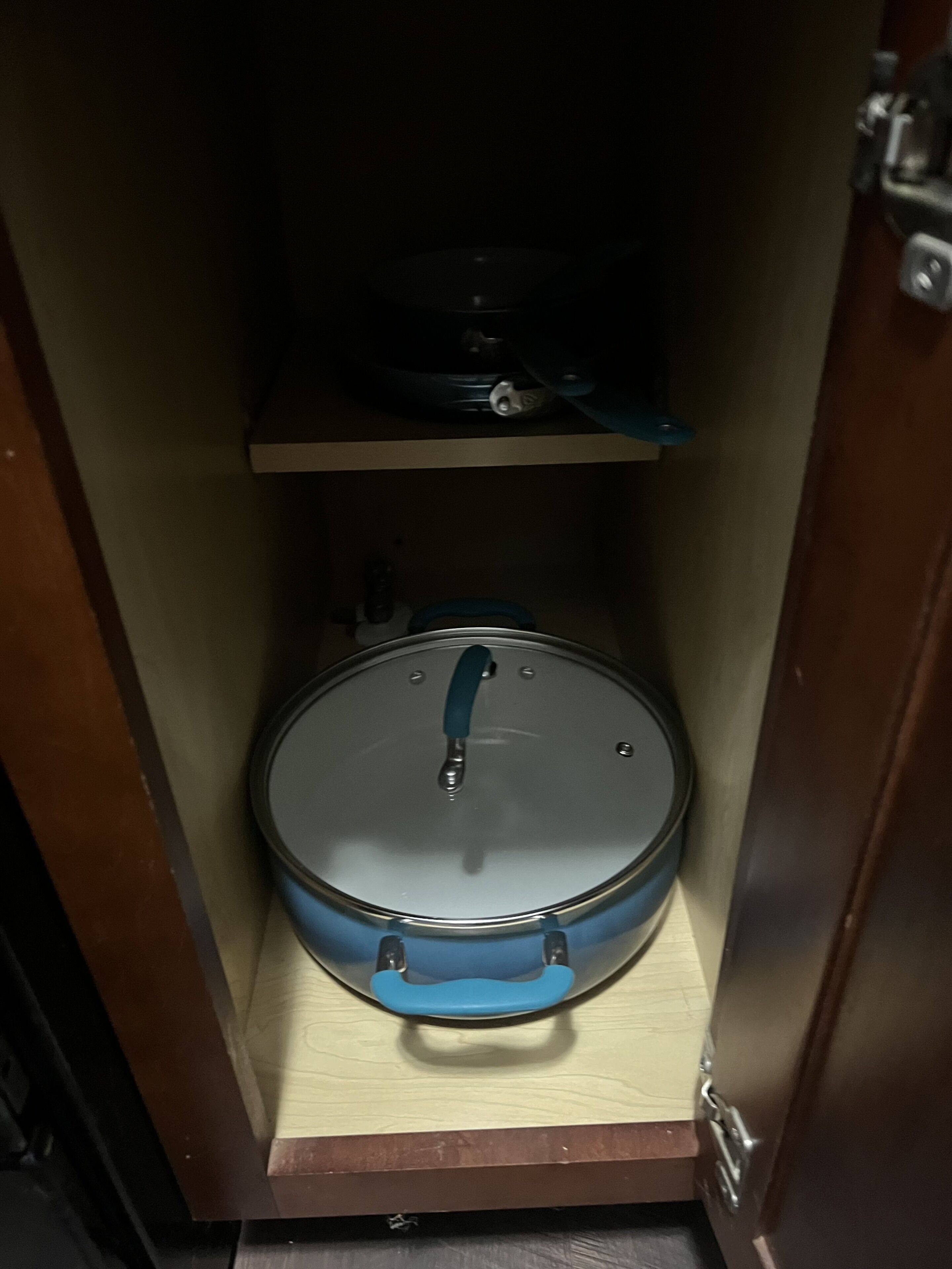 A compact storage space with a blue container and a lid, a shelf above, and a door with a lock.