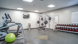 A gym with exercise equipment, a wall-mounted TV, and a rack of dumbbells.