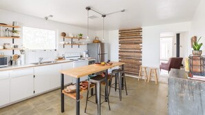 A modern kitchen with white cabinets, a wooden dining table, and a built-in stove.