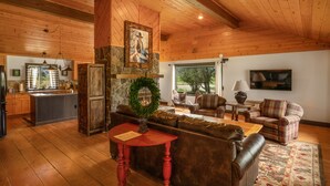 A cozy cabin interior with a stone fireplace, wooden ceiling, and a living area with a couch, chairs, and a coffee table. - Beautiful Log Farmhouse in Paradise Valley, Montana (Livingston)