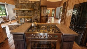 A kitchen with a stone fireplace, a gas stove, and a large black TV. - Beautiful Log Farmhouse in Paradise Valley, Montana (Livingston)