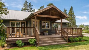 A log cabin with a wooden porch, steps leading to the entrance, and a view of the surrounding landscape. - Beautiful Log Farmhouse in Paradise Valley, Montana (Livingston)