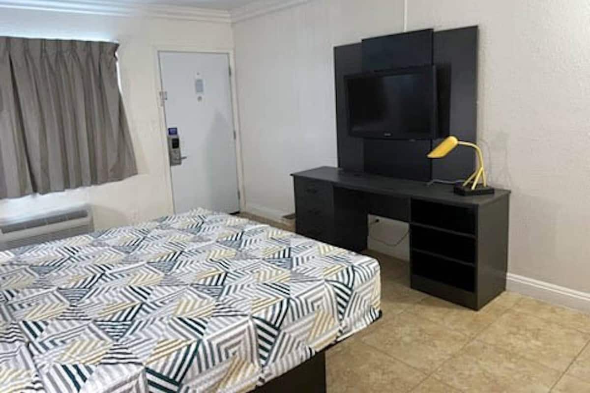 Ein Hotelzimmer mit einem Bett, einem Fernseher auf einem Standfuß, einem Schreibtisch und einer Lampe.