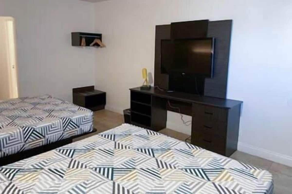Ein Schlafzimmer mit zwei Betten, einem Fernseher und einem Schreibtisch.