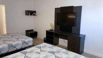 Quarto com duas camas, televisão e escrivaninha.