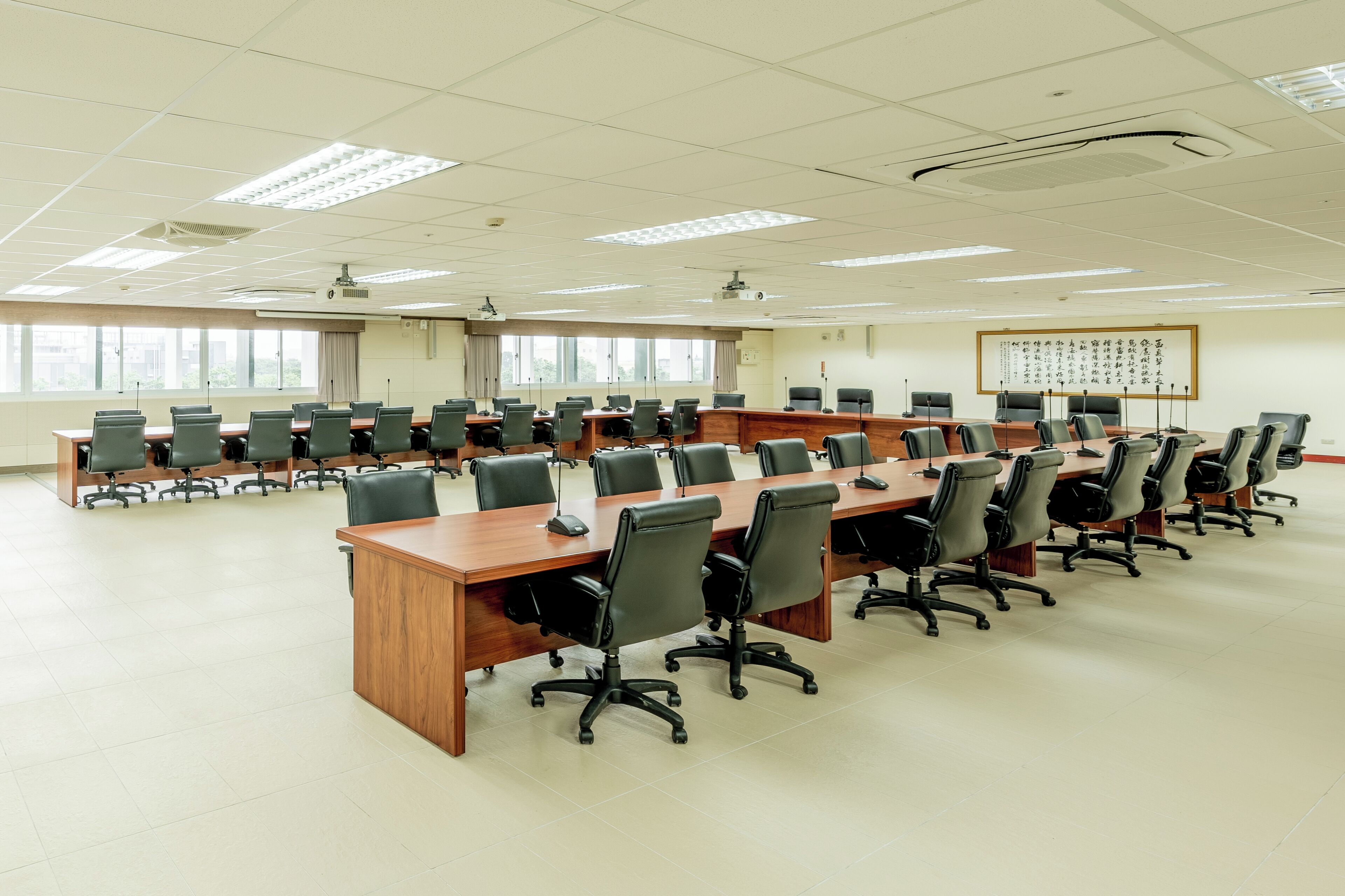 A conference room with multiple tables and chairs, large windows, and a projector screen.
