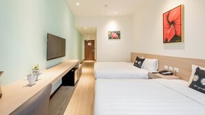 Une chambre d’hôtel avec deux lits, une télévision, un bureau avec un ordinateur et une petite plante.