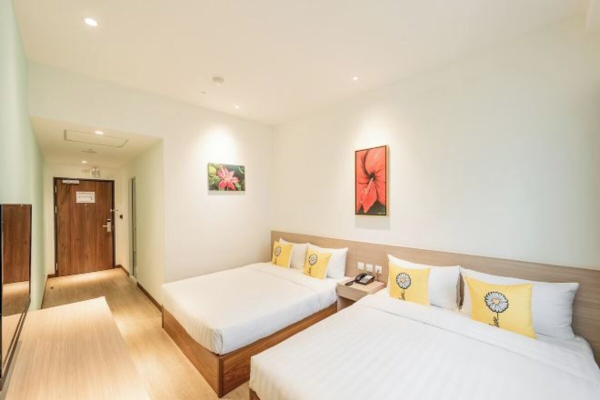 A hotel room with two beds, a wooden floor, a wooden door, and artwork on the walls.
