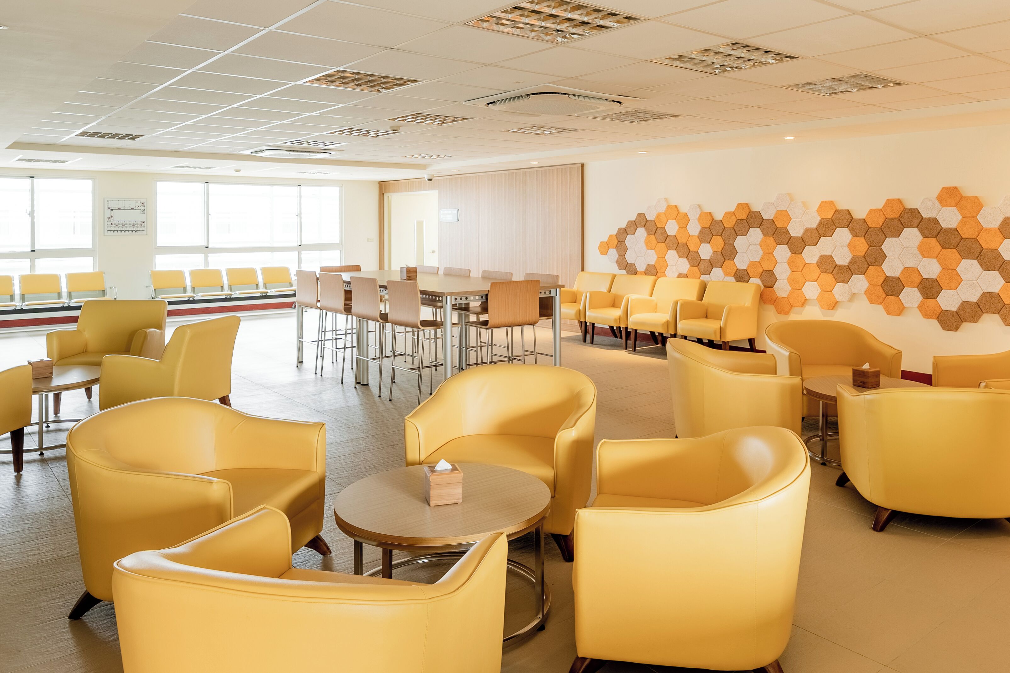 A spacious hotel lobby with yellow seating, a large table, and a wall with a geometric pattern.