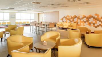 A spacious hotel lobby with yellow seating, a large table, and a wall with a geometric pattern.