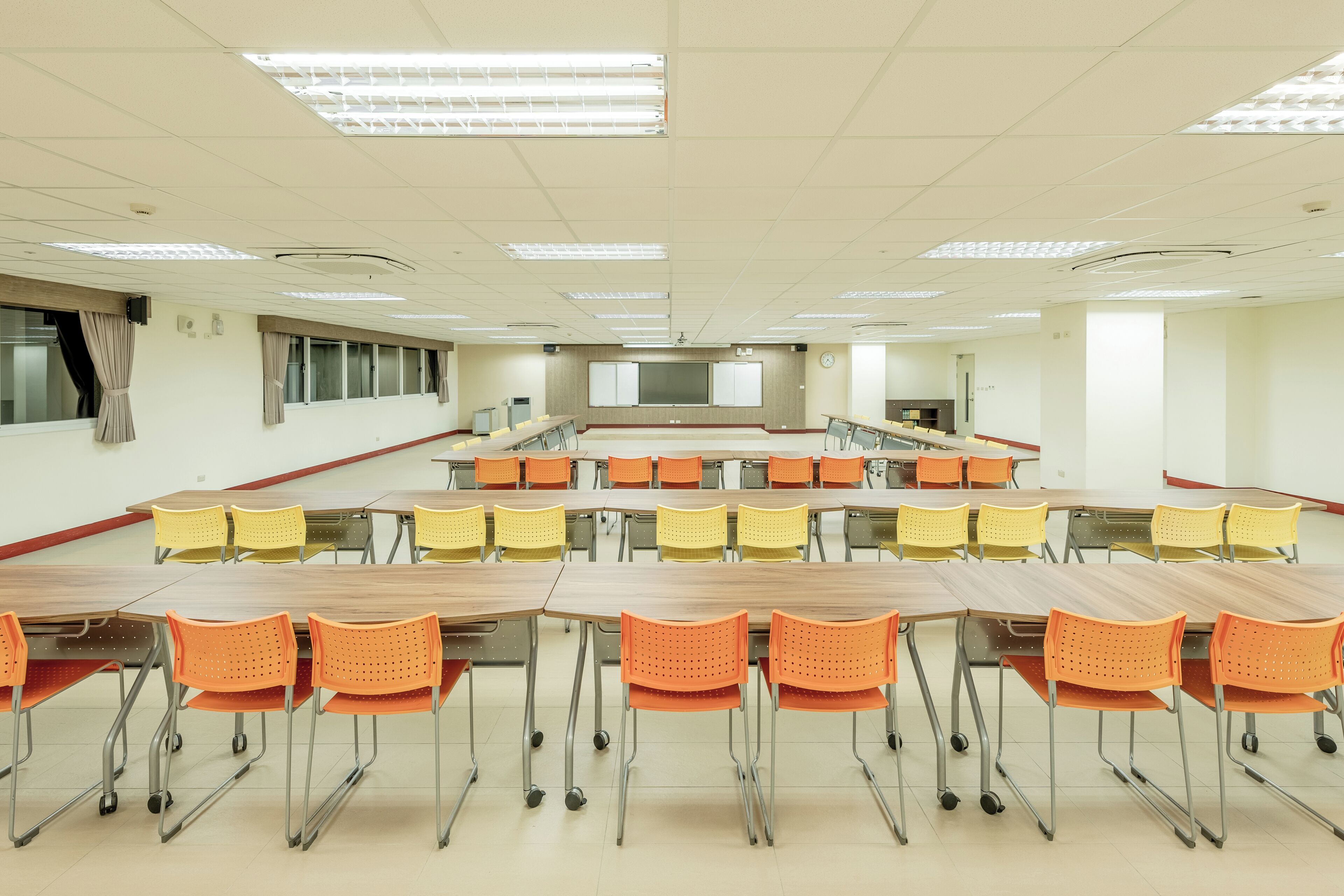 Une salle de classe avec des rangées de bureaux et de chaises, un écran de projection et une horloge au mur.