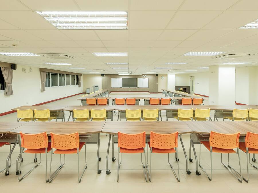Une salle de classe avec des rangées de bureaux et de chaises, un écran de projection et une horloge au mur.