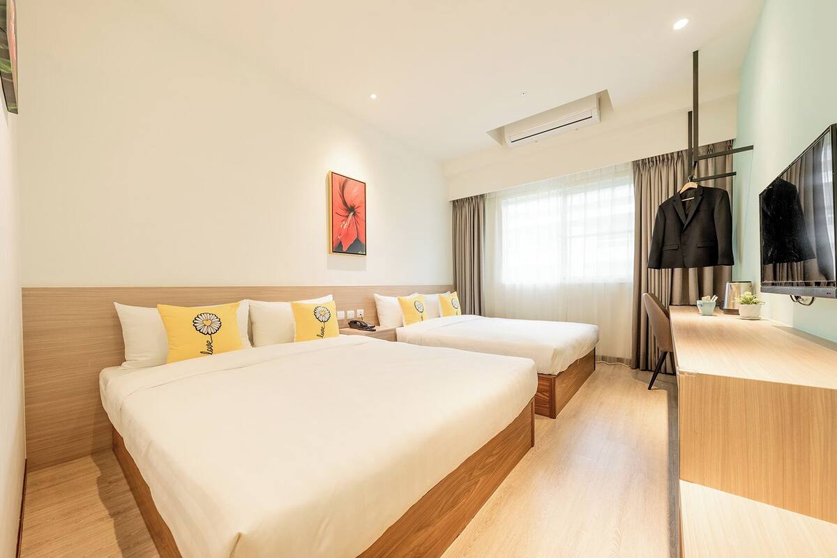 A hotel room with two beds, a desk, a TV, and a window with curtains.