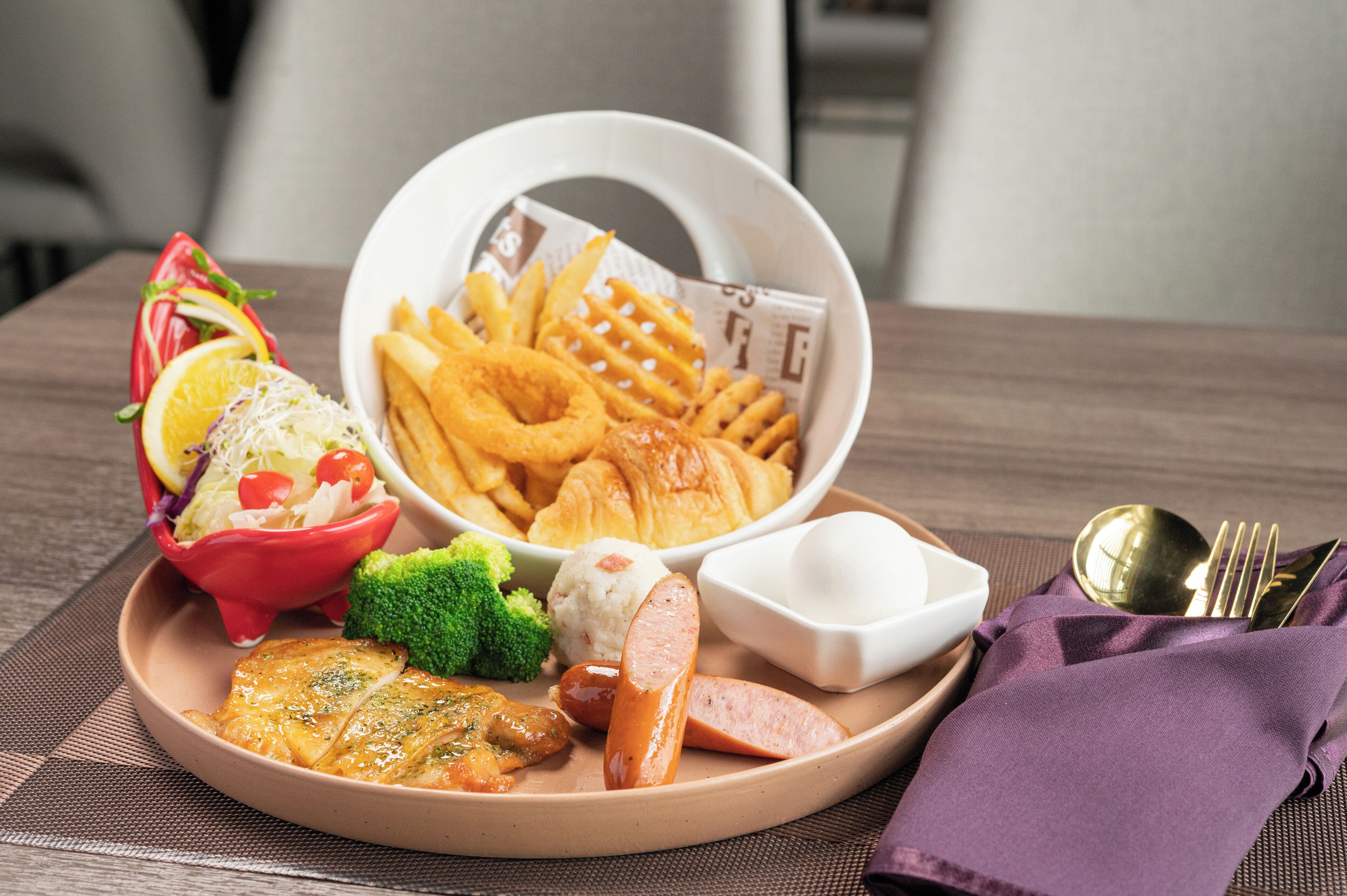 A plate with food including chicken, sausage, and fries, a bowl of onion rings, and a small salad.