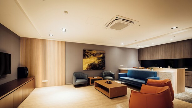 A modern living room with a sofa, coffee table, and chairs, a kitchen area with a blue sofa, and a flat-screen TV mounted on the wall. - TH Hotel (Changzhi)