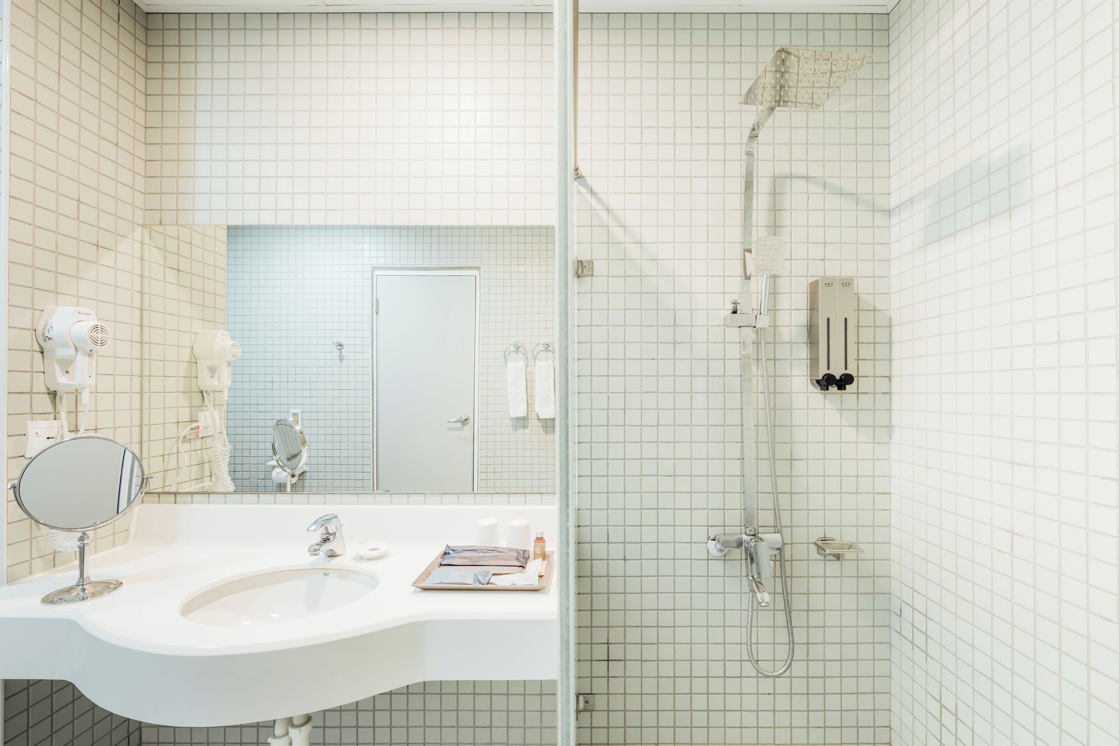 A bathroom with a white sink, mirror, and a shower area with a handheld showerhead.